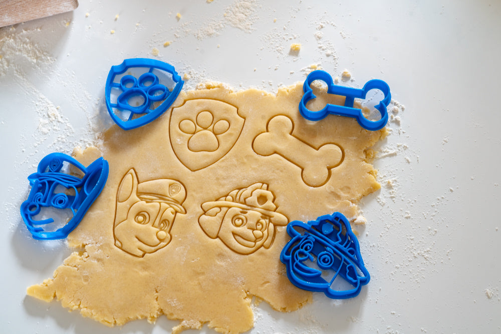 Empreintes de biscuits Pat’Patrouille réalisées avec des emporte-pièces Chase, Marcus, l’os et le badge patte sur une pâte à cookies.