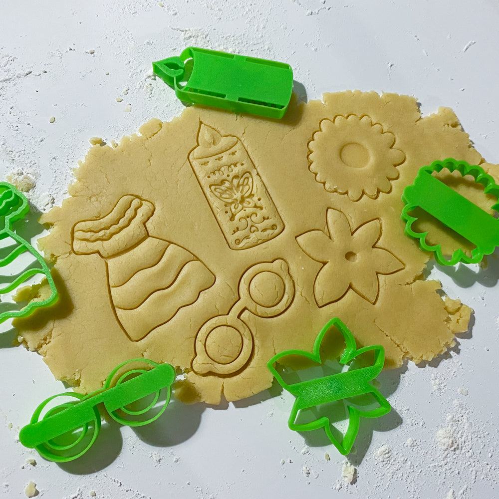 Emporte-pièces biscuit thème maison enchantée avec robe, bougie, lunettes et fleurs sur pâte à biscuits.