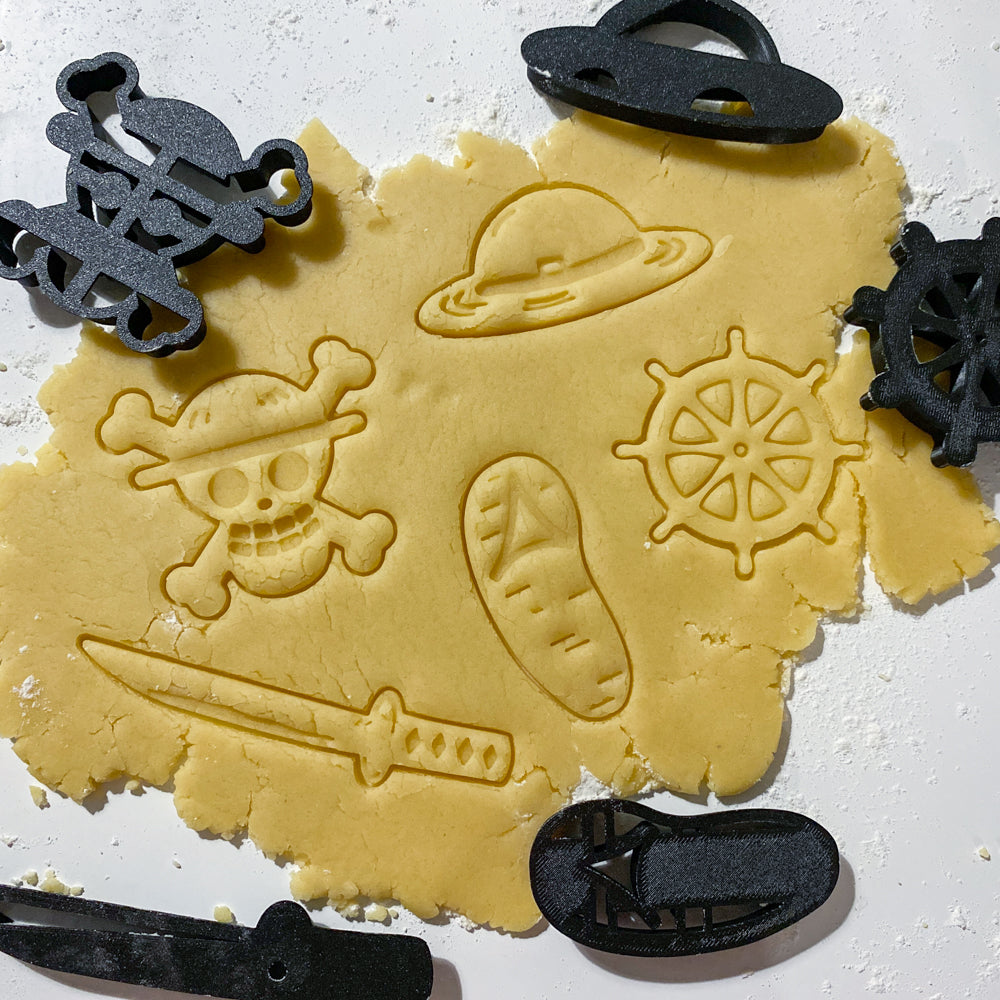 Emporte-pièces One Piece pour biscuits avec motifs chapeau pirate gouvernail tête de mort sabre et sandales imprimés dans la pate.
