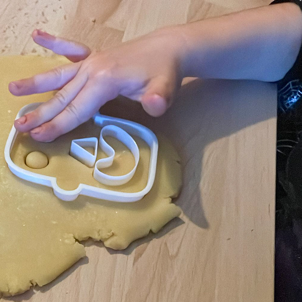 Enfant utilisant un emporte-pièce Halloween pour découper une tête de monstre dans une pâte à biscuits.