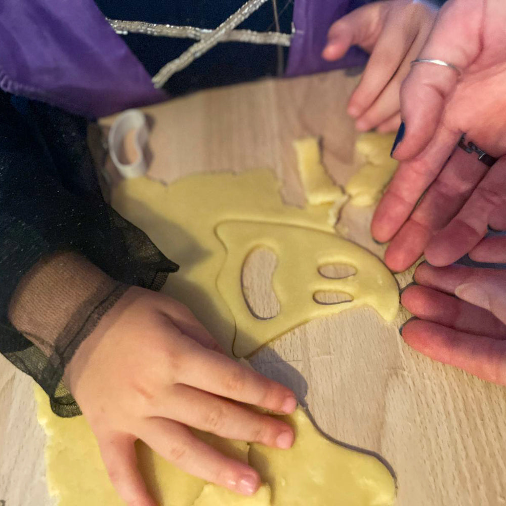 Enfant découpant un fantôme d’Halloween dans la pâte à biscuits avec l’aide d’un adulte.