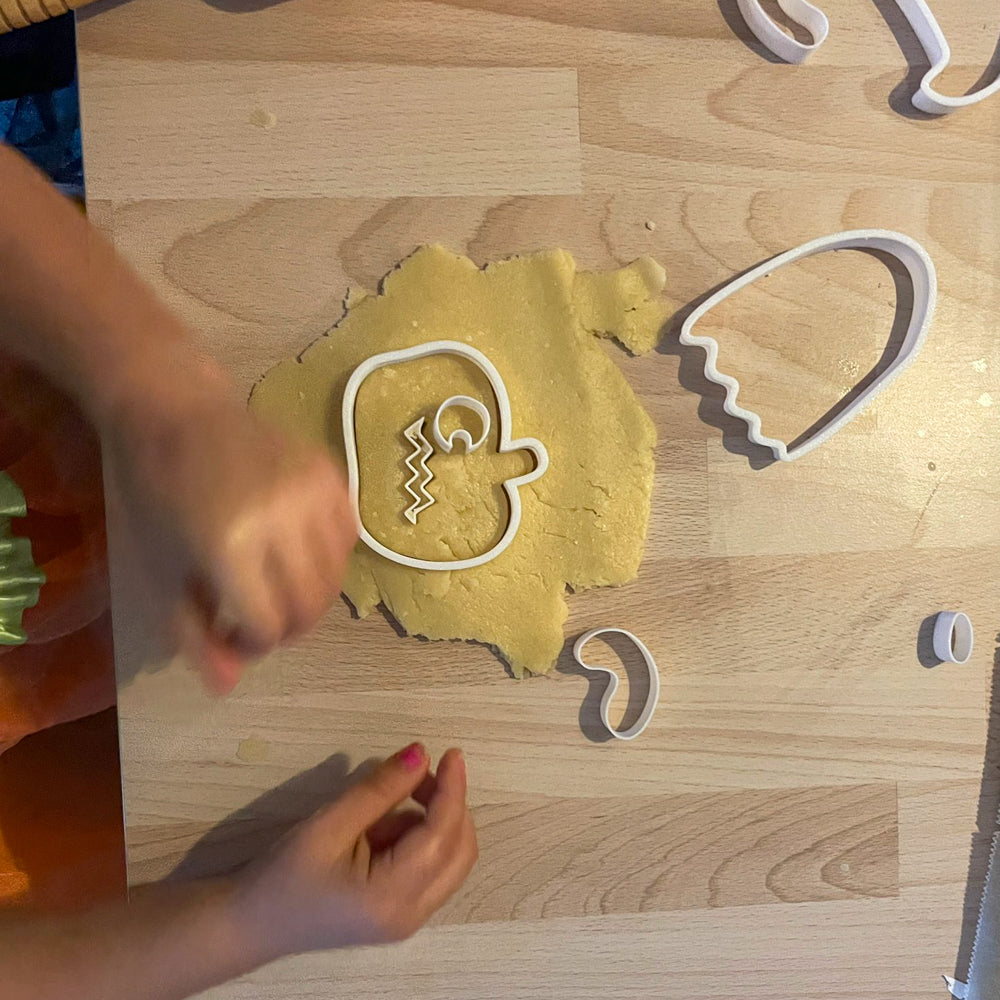 Enfant utilisant un emporte-pièce Halloween pour découper une tête de citrouille dans la pâte à biscuits.