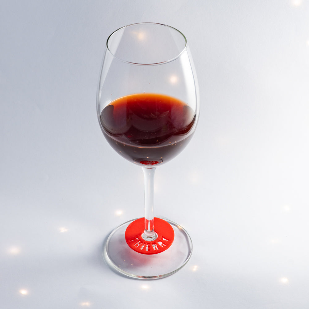 Verre à pied contenant du vin rouge, équipé d’un marque-verre creusé rouge placé autour du pied, avec le prénom “Thierry” découpé dans la pastille.