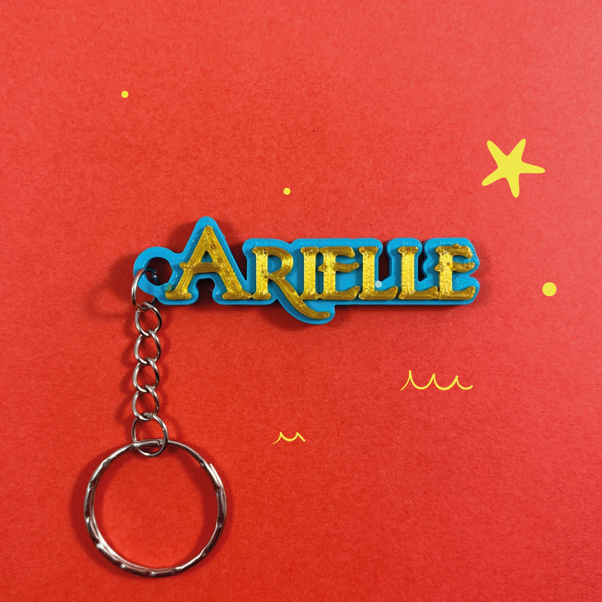 Porte-clés personnalisé bleu avec inscription en relief dorée au prénom Arielle sur fond rouge.