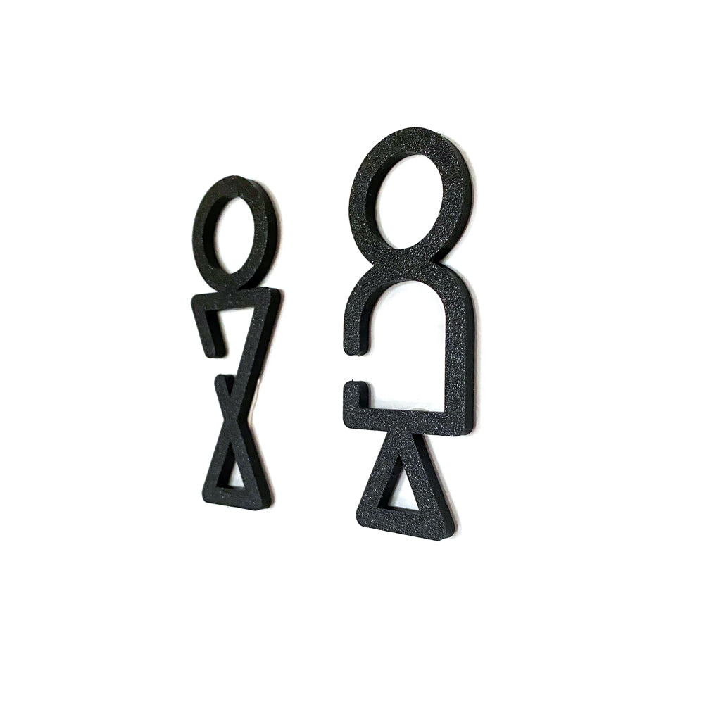 Pictogrammes noirs de toilettes homme et femme au style stylisé géométrique, en relief sur fond blanc, signalétique design pour porte de WC.